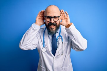 Poster - Handsome bald doctor man with beard wearing glasses and stethoscope over blue background Trying to hear both hands on ear gesture, curious for gossip. Hearing problem, deaf