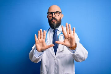 Wall Mural - Handsome bald doctor man with beard wearing glasses and stethoscope over blue background Moving away hands palms showing refusal and denial with afraid and disgusting expression. Stop and forbidden.