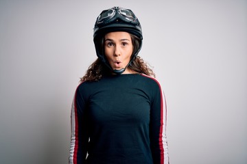 Sticker - Beautiful motorcyclist woman with curly hair wearing moto helmet over white background afraid and shocked with surprise expression, fear and excited face.