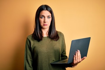 Wall Mural - Young brunette woman with blue eyes working using computer laptop over yellow background depressed and worry for distress, crying angry and afraid. Sad expression.