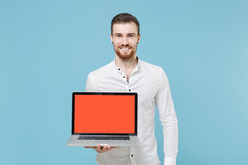 Smiling young bearded man guy 20s in white classic shirt isolated on pastel blue wall background studio. People lifestyle concept. Mock up copy space. Hold laptop pc computer with blank empty screen.