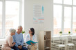 © Seventyfour - Wide angle portrait of young female doctor talking to senior couple while sitting in reception area of modern clinic, copy space