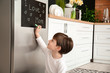 © Pixel-Shot - Little boy writing text I LOVE MOM on chalkboard in kitchen