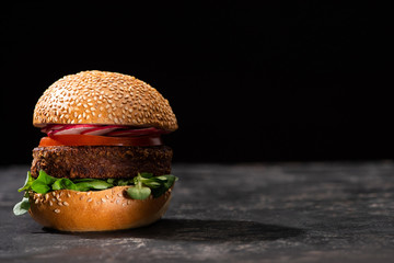 Tasty vegan burger with microgreens, radish and tomato served on textured surface isolated on black