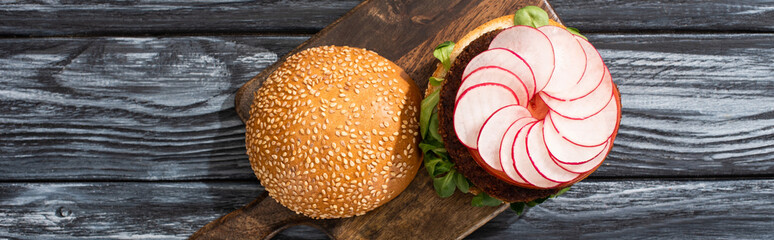 Wall Mural - top view of tasty vegan burger with microgreens, radish, tomato on cutting board served on wooden table, panoramic crop