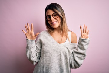 Canvas Print - Young beautiful brunette woman wearing casual sweater and glasses over pink background showing and pointing up with fingers number nine while smiling confident and happy.