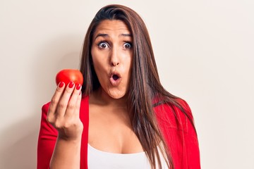 Sticker - Young beautiful brunette woman holding tomato scared and amazed with open mouth for surprise, disbelief face