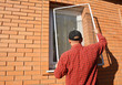 A man is installing anti-insect mosquito screen, net, mesh, resistant, insect protection on a window outdoors to keep flies, bugs and mosquitoes out of the house.