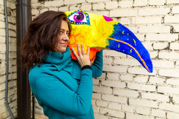 Young woman holding a mask of brightly colored bird head with a large beak. homemade original costume for the holiday.