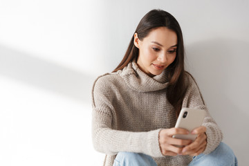 Poster - Image of pleased asian woman sitting and using smartphone