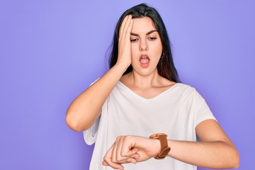 Poster - Young beautiful brunette woman wearing casual white t-shirt over purple background Looking at the watch time worried, afraid of getting late