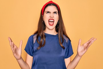 Sticker - Young beautiful brunette woman wearing red lips over yellow background crazy and mad shouting and yelling with aggressive expression and arms raised. Frustration concept.