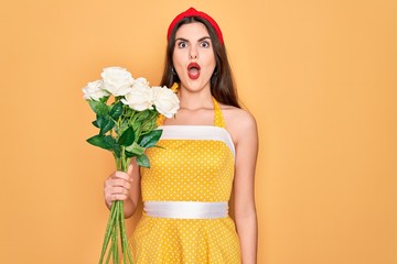 Sticker - Young beautiful pin up woman wearing 50s fashion vintage dress holding boquet of roses flowers scared in shock with a surprise face, afraid and excited with fear expression