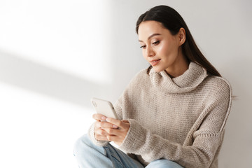 Wall Mural - Image of smiling asian woman sitting and using smartphone