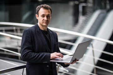 Wall Mural - Handsome businessman standing and holding laptop in office