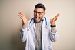 © Krakenimages.com - Young doctor man wearing glasses, medical white robe and stethoscope over isolated background celebrating mad and crazy for success with arms raised and closed eyes screaming excited. Winner concept