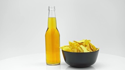 Wall Mural - bottle of light beer and chips in black bowl rotating on table isolated on white