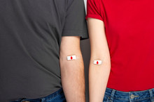 Blood Donorship. Man In Grey And Woman In Red T-shirt With Hands Taped Patch After Giving Blood With Red Drop