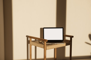 Wall Mural - Laptop with blank screen on wicker bench in sunlight shadows on the wall. Minimal interior design template with mockup copy space