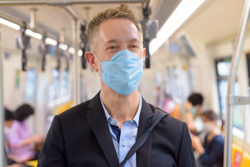 Sticker - Face of mature businessman with mask standing with distance inside the train