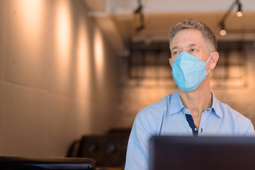 Canvas Print - Mature businessman with mask thinking while using laptop inside the coffee shop