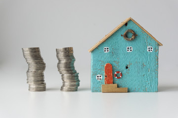 Beautiful blue small house with 2 rows of coins placed beside the house on a white background, real estate investment ideas.