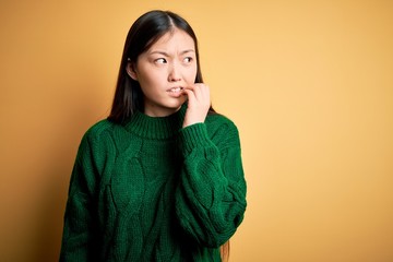 Sticker - Young beautiful asian woman wearing green winter sweater over yellow isolated background looking stressed and nervous with hands on mouth biting nails. Anxiety problem.