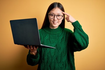 Poster - Young asian business woman wearing glasses and working using computer laptop Smiling pointing to head with one finger, great idea or thought, good memory