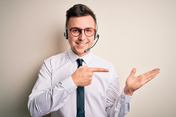 Wall Mural - Young handsome caucasian business man wearing call center headset at customer service amazed and smiling to the camera while presenting with hand and pointing with finger.