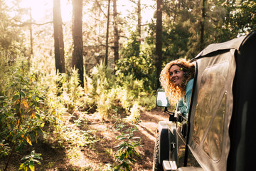 Alternative tourism people discover nature with off road car enjoying the forest and wood in the sunset sun light - cheerful happy woman outside the vehicle inside the wood