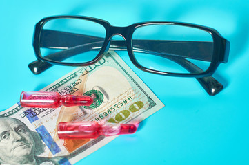 Wall Mural - Banknote of 100 usd, glasses and vaccine on green background. Corruption in medicine. Purchasing medications in pharmacy. Drugs donations. Payment for treatment. Health сare concept