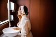 © Yakobchuk Olena - Happy female applying face cream in bathroom