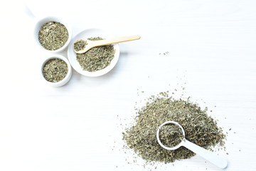 Chopped dried leaves of basil leaves on white wooden background