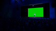 © Gorodenkoff - Keynote Speaker Does Presentation of New Product to the Audience, Behind Him Movie Theater with Green Screen, Mock-up, Chroma Key. Business Conference Live Event or Device Reveal