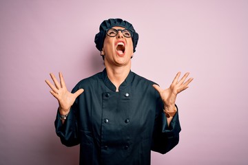 Sticker - Middle age brunette chef woman wearing cooker uniform and hat over isolated pink background crazy and mad shouting and yelling with aggressive expression and arms raised. Frustration concept.