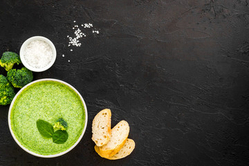 Wall Mural - Broccoli cream soup, bread, spoon on black kitchen desk top-down space for text