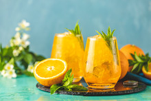 Two glass of orange ice drink with fresh mint on wooden turquoise table surface. Fresh cocktail drinks with ice fruit and herb decoration. Alcoholic non-alcoholic beverage