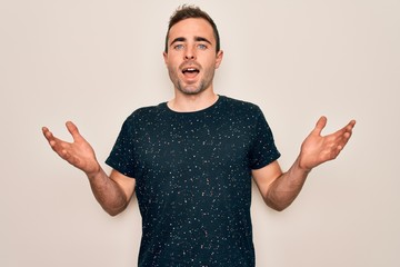 Wall Mural - Young handsome man with blue eyes wearing casual t-shirt standing over white background celebrating crazy and amazed for success with arms raised and open eyes screaming excited. Winner concept