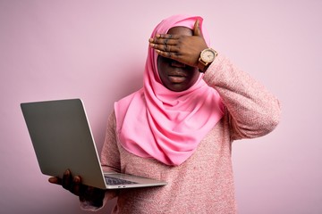 Poster - African american plus size woman wearing muslim hijab using laptop over pink background covering eyes with hand, looking serious and sad. Sightless, hiding and rejection concept