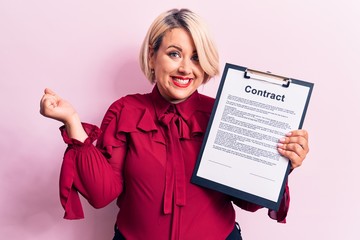 Wall Mural - Young beautiful blonde plus size woman holding clipboard with contract document paper screaming proud, celebrating victory and success very excited with raised arm