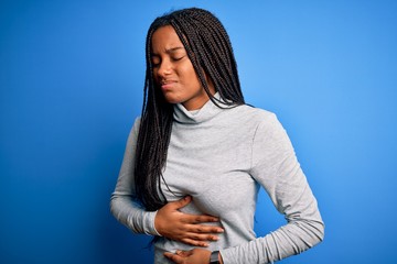 Sticker - Young african american woman standing wearing casual turtleneck over blue isolated background with hand on stomach because indigestion, painful illness feeling unwell. Ache concept.