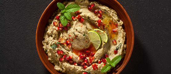 Wall Mural - banner of homemade spread of baked eggplant baba ganoush in a bowl with pomegranate seeds, lime, olive oil and lime slices on a black background