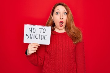 Sticker - Beautiful redhead woman holding banner showing no to suicide message over red background scared in shock with a surprise face, afraid and excited with fear expression