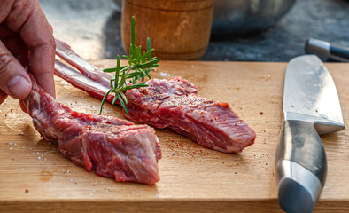 Man's hand holding lamb chops with rosemary and spices and big knife on wooden cutting board