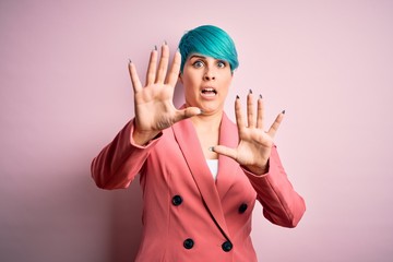 Sticker - Young beautiful businesswoman with blue fashion hair wearing jacket over pink background afraid and terrified with fear expression stop gesture with hands, shouting in shock. Panic concept.