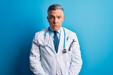 Poster - Middle age handsome grey-haired doctor man wearing coat and blue stethoscope depressed and worry for distress, crying angry and afraid. Sad expression.