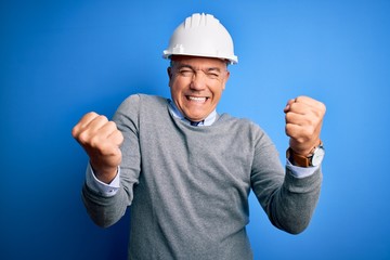 Sticker - Middle age handsome grey-haired engineer man wearing safety helmet over blue background very happy and excited doing winner gesture with arms raised, smiling and screaming for success. Celebration