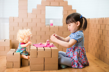 Wall Mural - toddler girl pretend play baby care in a cardboard block house