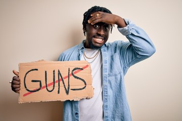 Sticker - Young african american man asking for peace holding banner with prohibited guns message stressed with hand on head, shocked with shame and surprise face, angry and frustrated. Fear and upset