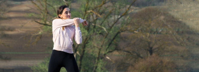 A young slim athletic girl in sportswear performs a set of exercises. Fitness and healthy lifestyle  against the background of green spring pasture hills.